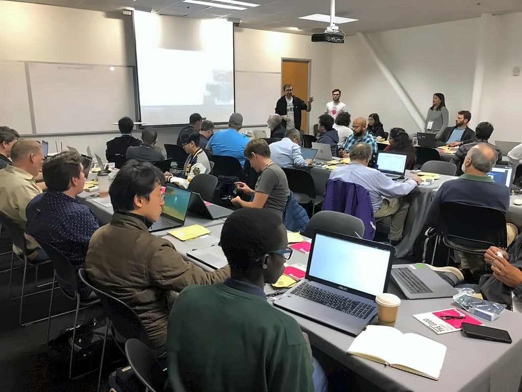A second workshop room mid-session, attendees at laptops with presenters working the room