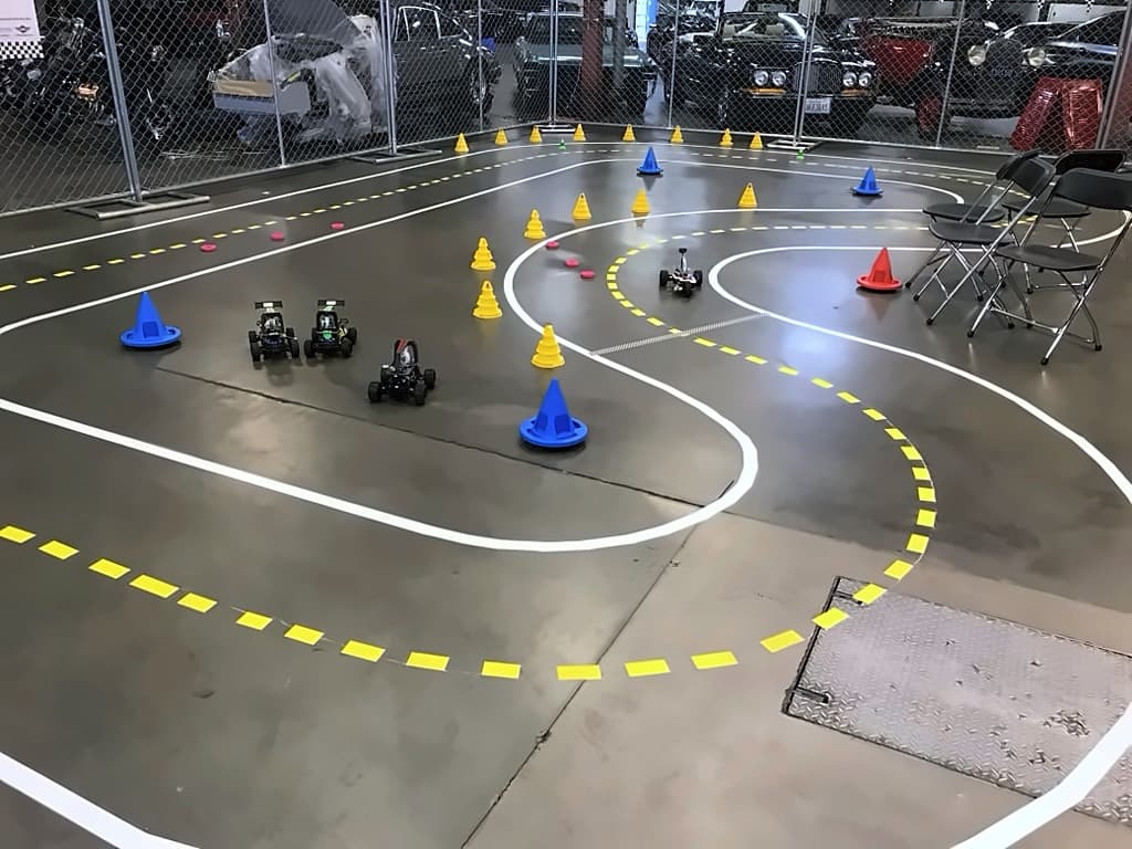The taped autonomous vehicle course with cones, and four small self-driving cars on the concrete floor