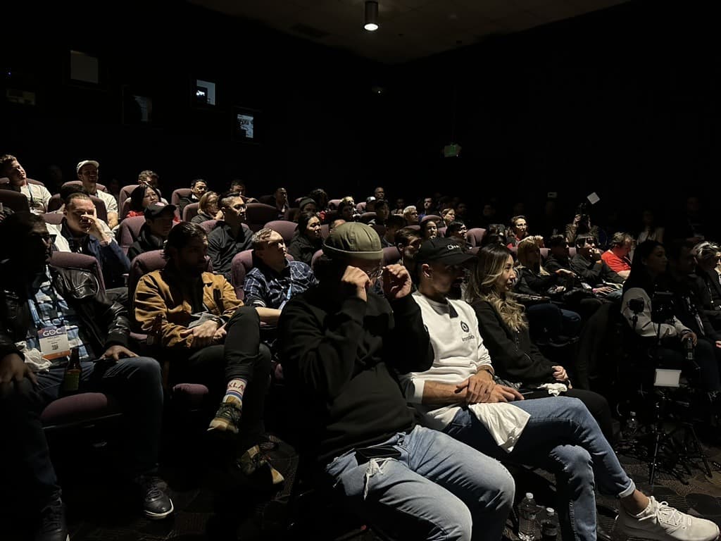 A full cinema auditorium during the premiere, attendees in raked seating with GDC badges on their lanyards